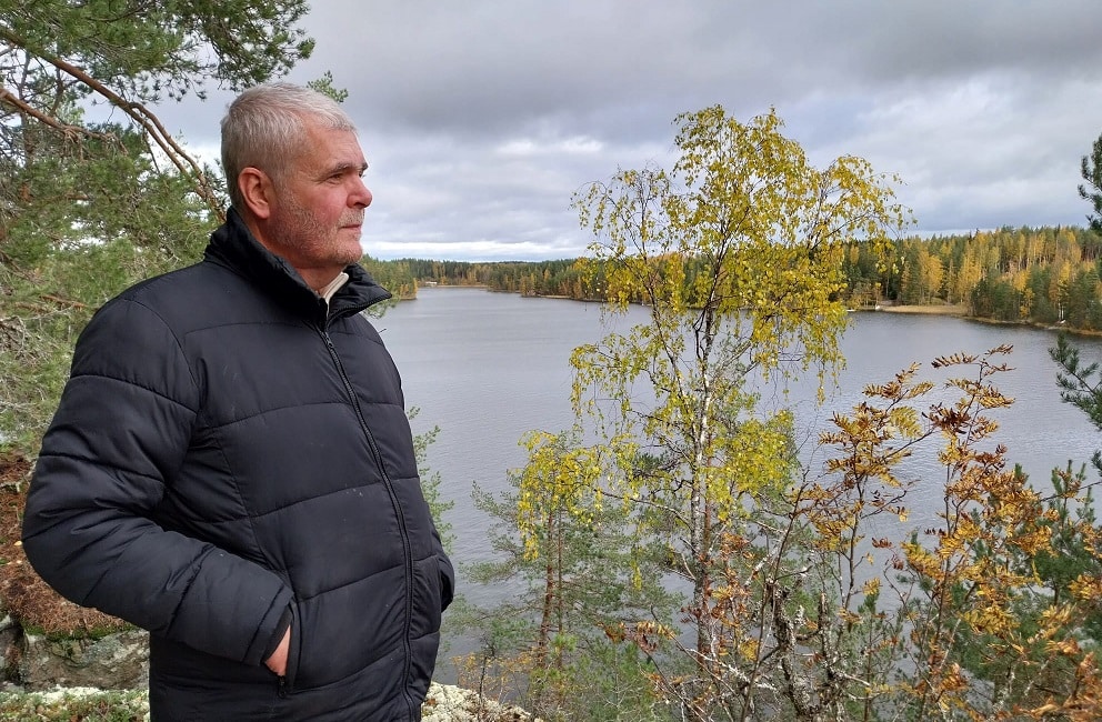 Mies seisoo kalliolla, katsoo syksyistä järveä.