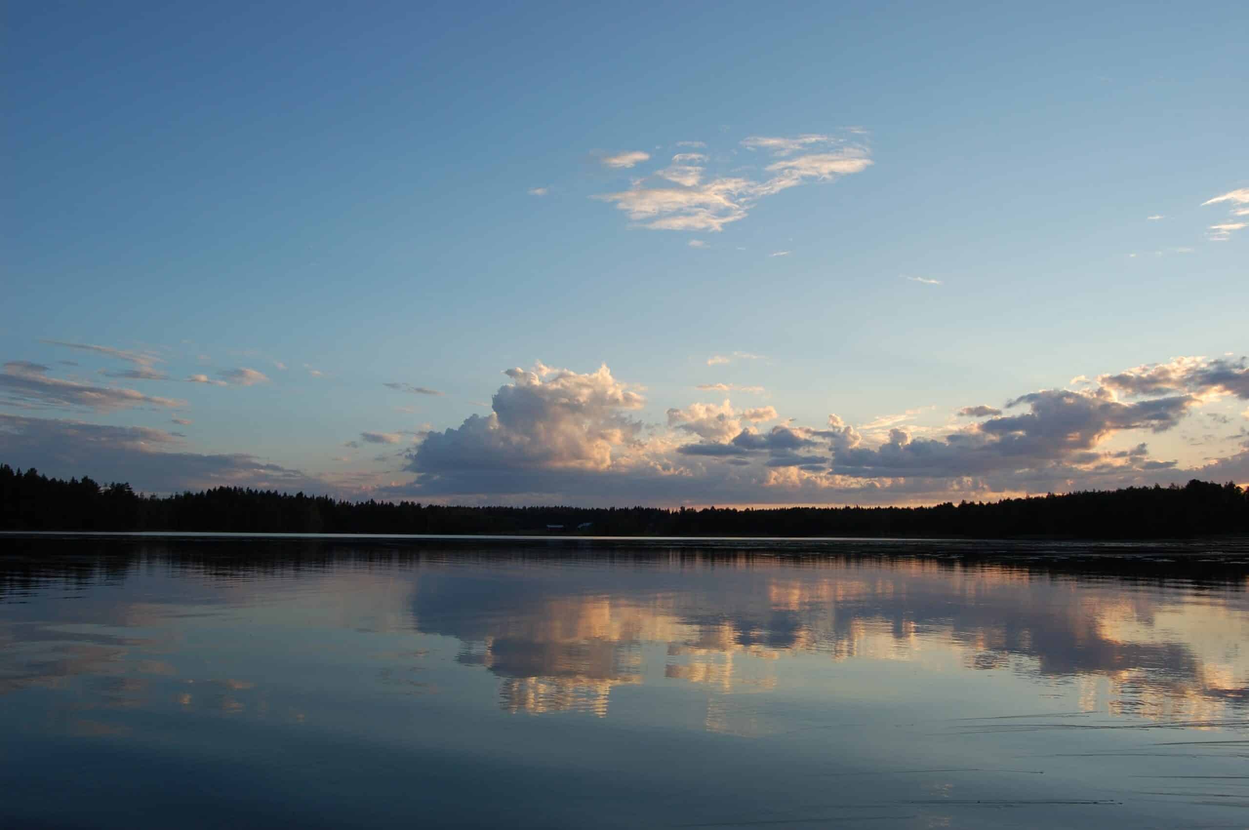 Pilvien kuvajainen tyynen järven pinnalla.