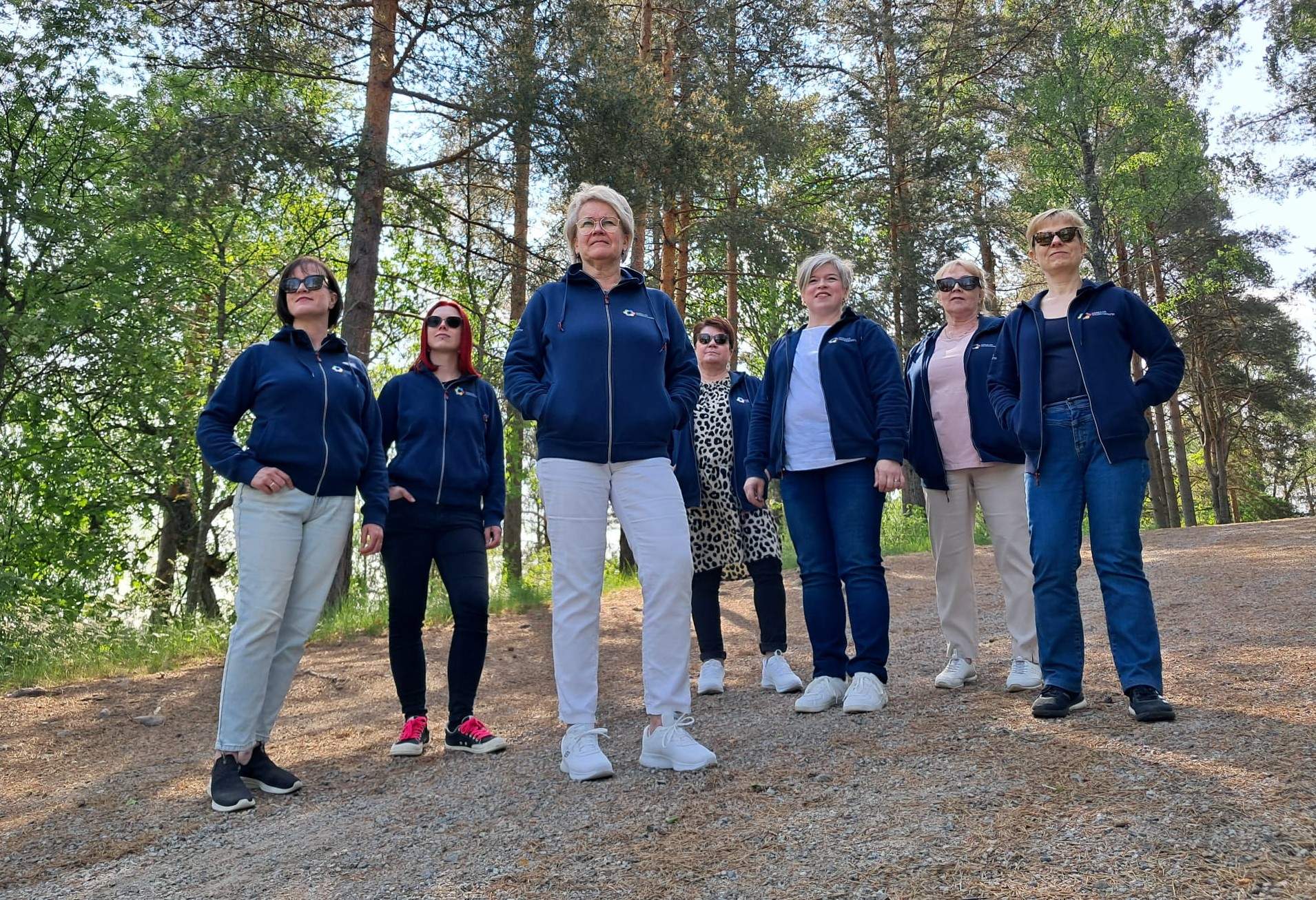 Saimaan Syöpäyhdistyksen työntekijät seisovat metsätien rinteessä katsoen kaukaisuuteen.