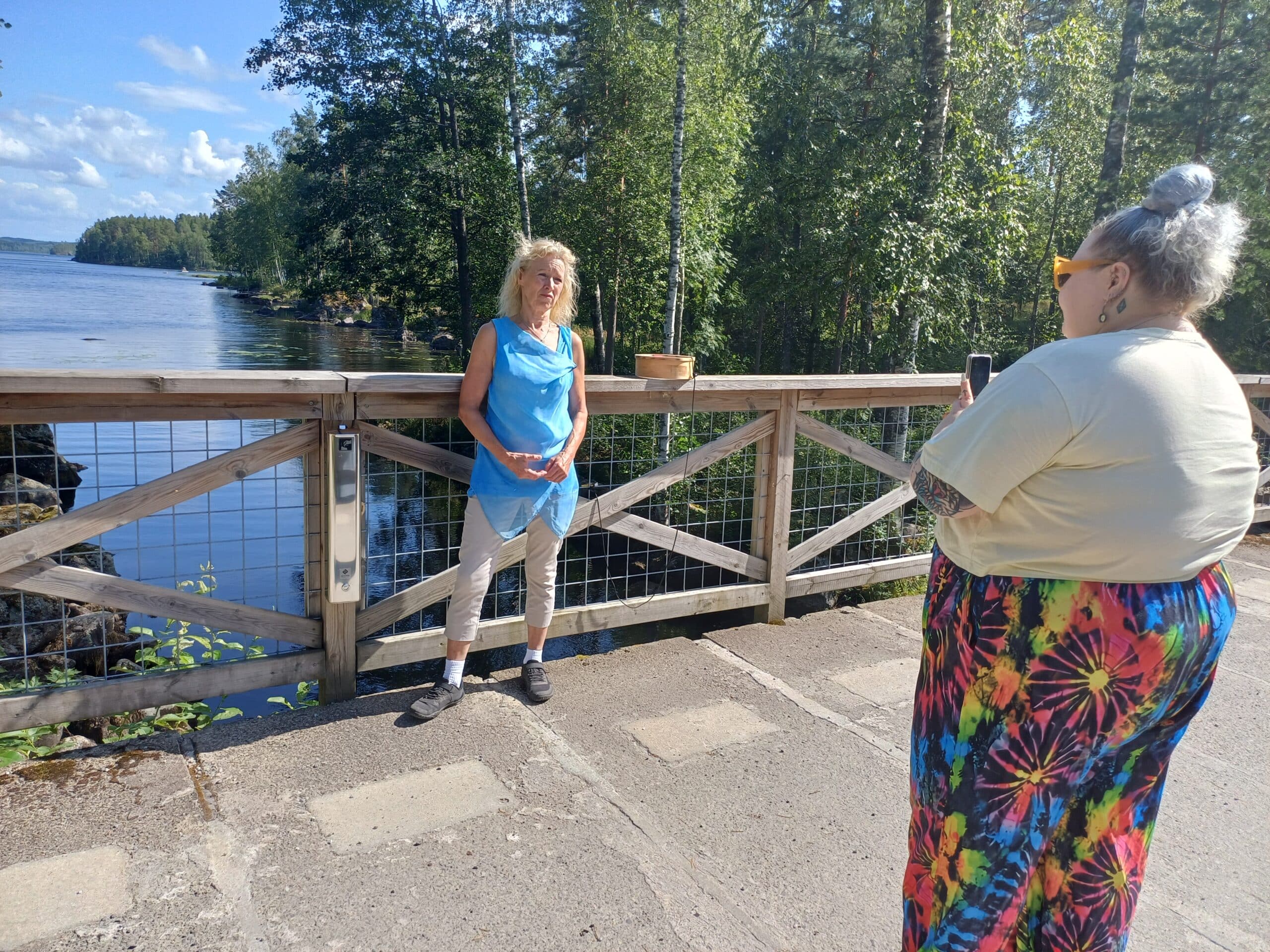 Kaksi naista seisoo sillalla, nuorempi kuvaa puhelimella vanhempaa.