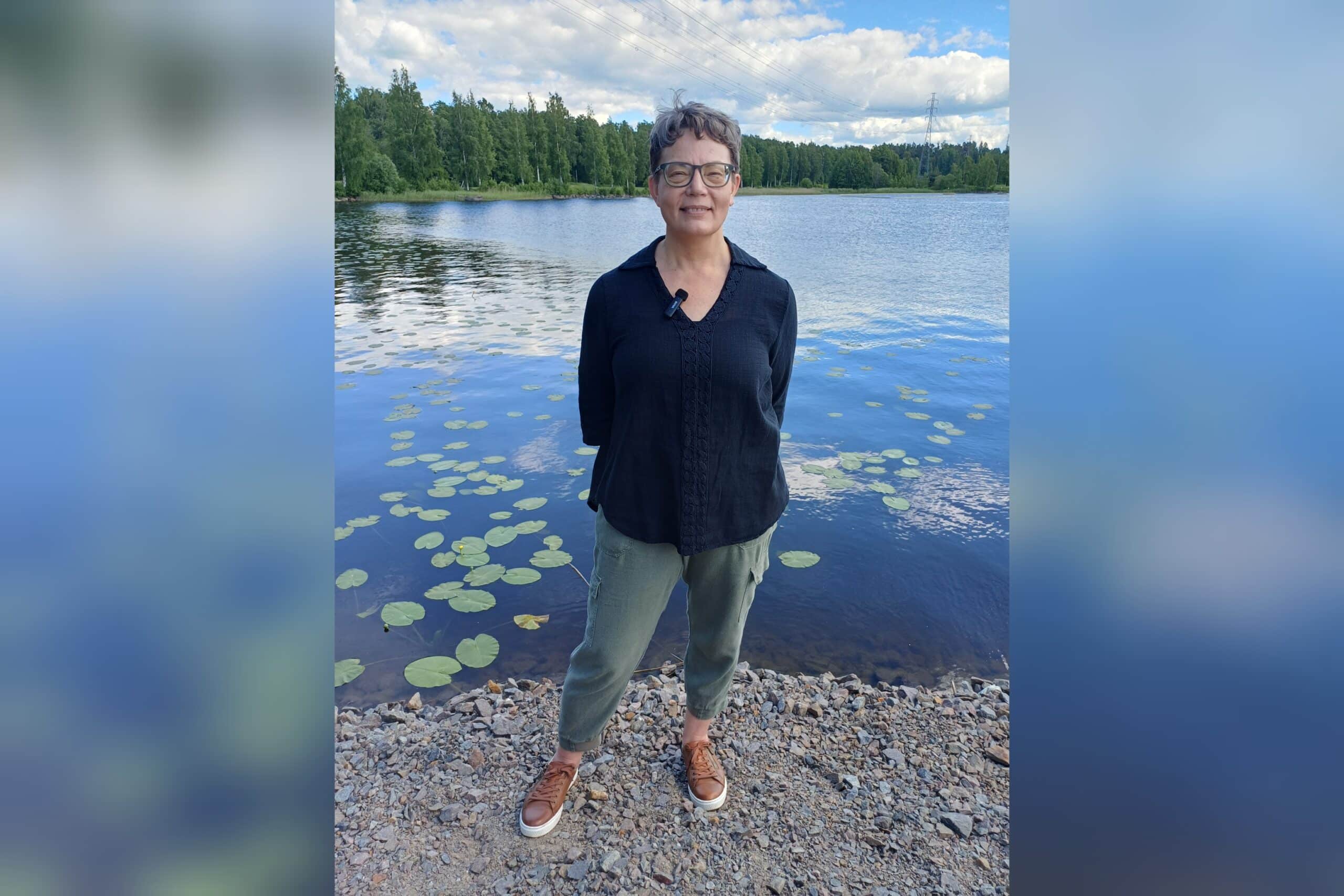 Kokemustoimija Kristiina seisoo kesäisen järven rannalla.